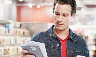 Young man shopping and deciding whether to buy the latest CD while holding multiple shopping bags and a latte.