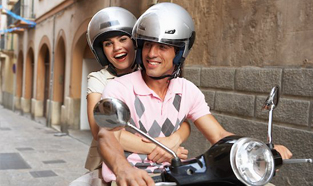 Jeune couple, portant des casques, roulant sur une rue tranquille en mobylette.